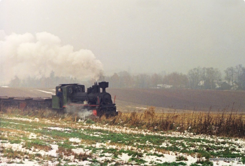 Fotografie Mezi loukami a poli stoupá parní vlak z&nbsp;Mladějova.