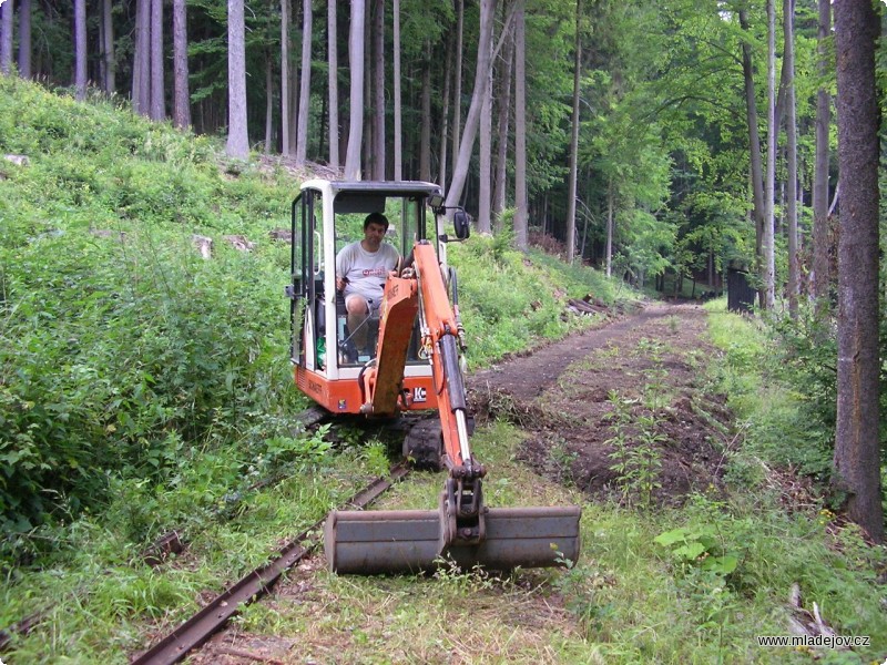 Fotografie Bagr připravuje místo pro novou trať, v&nbsp;pozadí se pracuje na pokládání kolejí, které jde mnohem pomaleji.