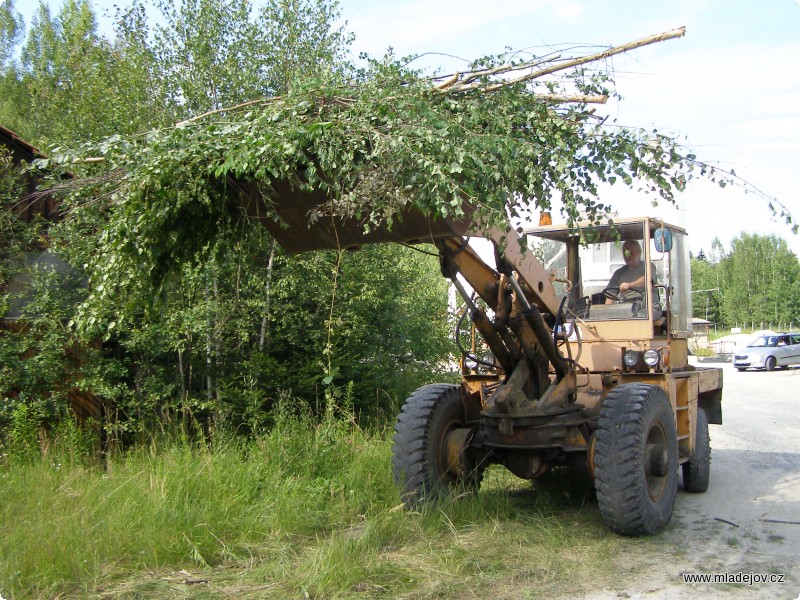 Fotografie Hromady křoví odváží hydraulický nakladač.
