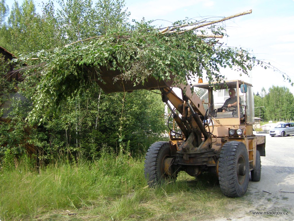 Fotografie Hromady křoví odváží hydraulický nakladač.
